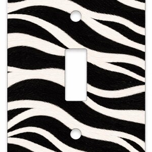 May include: A rectangular light switch wall plate featuring a black and white zebra stripe pattern. The cover has a central vertical rectangular cutout for a toggle switch and two circular screw holes positioned at the top and bottom centers.