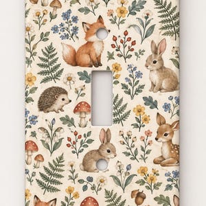 May include: A rectangular light switch cover plate featuring a cream-colored background with a repeating pattern of woodland animals including foxes, rabbits, a hedgehog, and a fawn, interspersed with mushrooms, ferns, and various wildflowers.