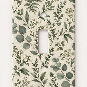 May include: A rectangular light switch wall plate featuring a botanical pattern of white flowers, green eucalyptus leaves, and fern fronds on a cream-colored background. The plate has a central rectangular cutout and two circular screw holes.