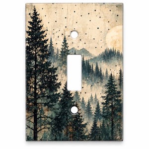 May include: A rectangular light switch cover plate featuring a printed forest landscape with dark green pine trees, distant mountains, a pale moon, and scattered black dots against a textured, cream-colored background with two screw holes.