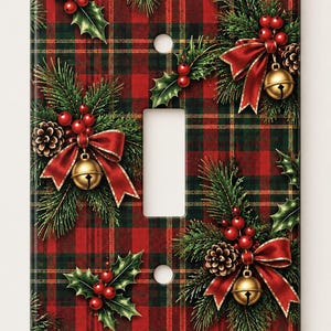 May include: A rectangular light switch cover plate featuring a red and green plaid pattern. The design is decorated with repeating clusters of green pine needles, brown pinecones, red holly berries, gold jingle bells, and red ribbons.