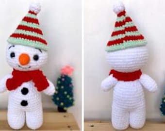 May include: A white crocheted snowman doll featuring a bright orange carrot-shaped nose, two black circular buttons on the torso, and a red scarf. The snowman wears a pointed hat with horizontal red and light green stripes and a white pom-pom.