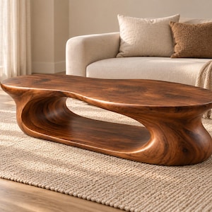 May include: A low-profile coffee table crafted from solid dark brown wood with a smooth, organic, and fluid shape. The table features a continuous, curved design with a large, hollow open space in the centre, creating a sculptural silhouette.
