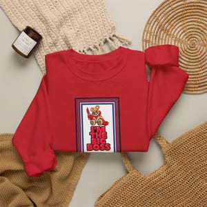 Könnte beinhalten: Ein rotes langärmeliges Sweatshirt mit Rundhalsausschnitt und einem Grafikdruck eines braunen Teddybären, der ein Messer mit roten Akzenten hält. Der Bär befindet sich über dem Text I'M THE BIG BOSS in fetten roten Buchstaben, umrahmt von einem Rand.