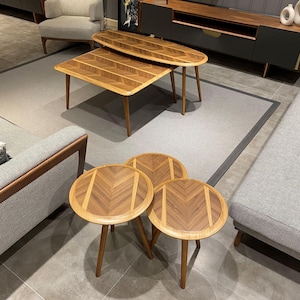 Op de afbeelding: Een set van vijf houten tafels met een natuurlijke houtnerf en een visgraatpatroon op de tafelbladen. De collectie bevat twee rechthoekige tafels met afgeronde hoeken en drie ronde tafels, allemaal ondersteund door taps toelopende houten poten.