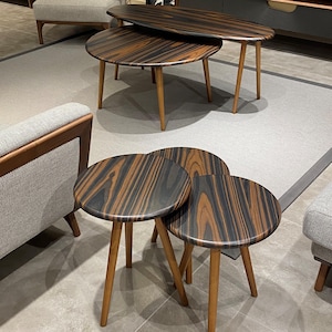 May include: A set of five nesting tables featuring circular and oval tops with a dark brown and black striped wood grain pattern. Each table is supported by three tapered light brown wooden legs, creating a tiered arrangement of surfaces.