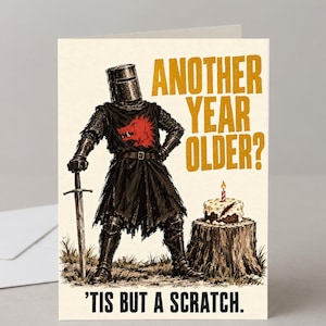 May include: A greeting card featuring a knight in black armour with a red boar emblem on the chest, holding a sword. Next to the knight is a birthday cake on a tree stump. Text reads: ANOTHER YEAR OLDER? and 'TIS BUT A SCRATCH.