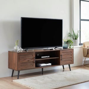 May include: A rectangular brown wood media console with two louvered cabinet doors, black metal handles, and four tapered black legs. The unit features an open center shelf containing a black electronic device and a book titled David Lynch.