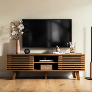 May include: A rectangular wooden media console featuring horizontal slatted doors on both sides and an open central shelving unit. The console stands on four tapered legs and holds a television, a vase with white flowers, and decor.