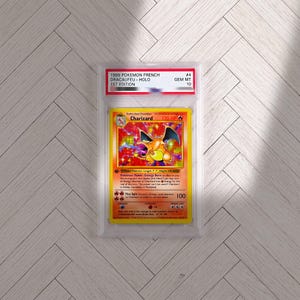 Puede incluir: Una carta coleccionable Pokemon Charizard de la 1ª edición francesa de 1999 encapsulada en una funda de plástico transparente PSA. La carta presenta una ilustración holográfica del dragón naranja, 120 HP y el texto 1999 POKEMON FRENCH DRACAUFEU-HOLO.