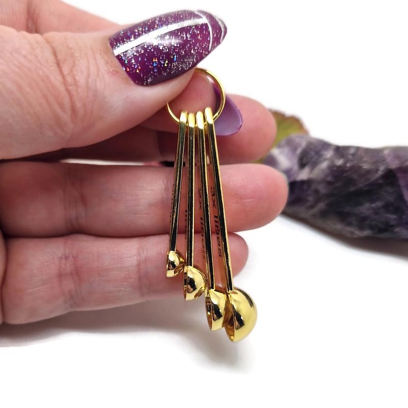 Puede incluir: Un juego de cinco cucharaditas medidoras doradas con un anillo para mantenerlas juntas. Las cucharaditas est&aacute;n etiquetadas con medidas en cucharaditas y cucharadas.