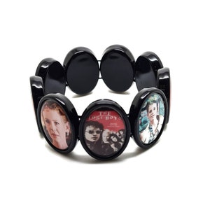 Può includere: Braccialetto elastico nero con ciondoli rotondi di forma ovale che mostrano immagini del film "The Lost Boys".