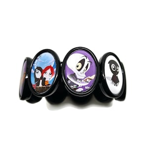 May include: Black bracelet with four round, colorful buttons featuring cartoon characters. The buttons are attached to a black elastic band.
