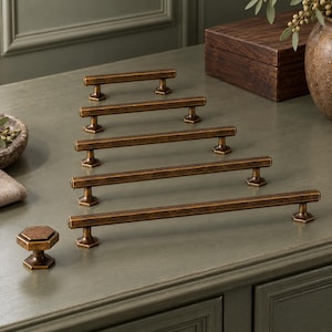 May include: A collection of five metal cabinet pulls and one matching hexagonal cabinet knob. Each piece features a dark, weathered bronze finish with a distinct hexagonal profile and faceted ends, arranged in a graduated size sequence.