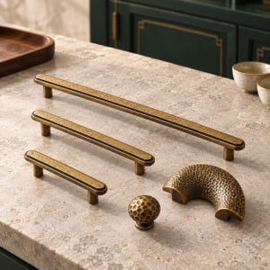 May include: A collection of antique brass hardware including three linear bar pulls of varying lengths, one spherical knob with a hammered texture, and one semi-circular drawer pull featuring a matching hammered finish and dark edges.