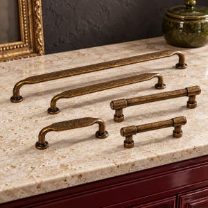 May include: A collection of five metal cabinet pulls in a dark, weathered bronze finish. The set includes three elongated pulls with a flat, tapered center bar and two cylindrical pulls with a smooth, rounded design, all featuring circular bases.