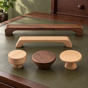 May include: A collection of wooden cabinet hardware including two long rectangular drawer pulls and three circular knobs. One pull and one knob are made of dark brown wood, while the other pull and two knobs are made of light tan wood.