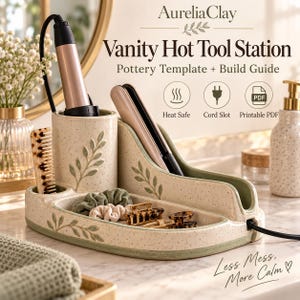 May include: A ceramic vanity hot tool station with a speckled cream finish and green leaf accents. It features a cylindrical holder for a curling iron, a slanted slot for a flat iron, and a tray for hair accessories. Text reads: AureliaClay Vanity Hot Tool Station Pottery Template + Build Guide.
