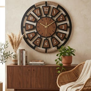 May include: A large circular wall clock featuring a dark black frame with natural rope accents at the top and bottom. The clock face has a central wood-toned circle with gold hands and twelve trapezoidal wood-toned segments displaying numbers 1-12.