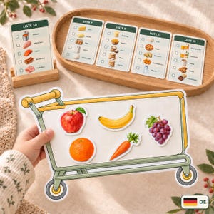 Könnte beinhalten: Ein Einkaufswagen-Spielbrett mit fünf Lebensmittelaufklebern: ein roter Apfel, eine gelbe Banane, eine lila Weintraube, eine Orange und eine Karotte. Dahinter liegen auf einem Holztablett fünf rechteckige Karten mit der Aufschrift LISTE 7, 8, 10, 11 und 12.