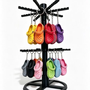 May include: A black rotating display stand featuring two tiers of metal hooks, each holding a miniature clog-style shoe keychain. The keychains come in a variety of vibrant colours including yellow, orange, red, purple, grey, black, pink, green, and blue.
