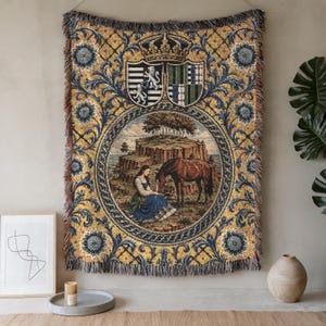 May include: A woven wall tapestry featuring a central circular scene of a person in a blue dress with a brown horse near a rocky cliff. The design includes a crown, two heraldic shields, and ornate floral patterns in gold, blue, and cream.