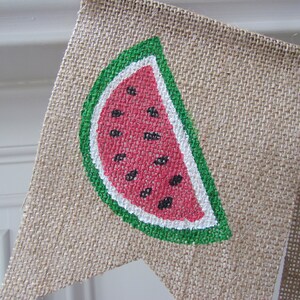 May include: A burlap banner with a painted watermelon slice. The watermelon is red with black seeds and a green rind.