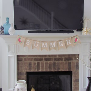 May include: A burlap banner with the word "SUMMER" in white letters and watermelon graphics hangs above a brick fireplace.