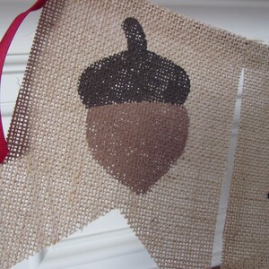 May include: A burlap banner with a brown acorn design and the word "Fall" in black lettering.