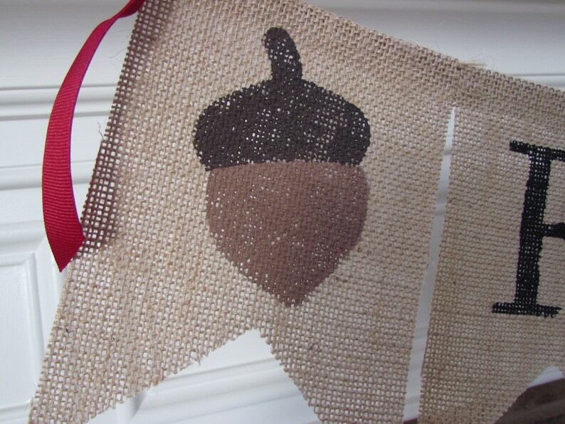 May include: A burlap banner with a brown acorn design and the word "Fall" in black lettering.