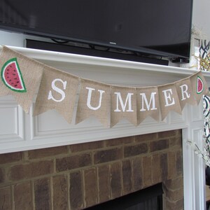 May include: A burlap banner with the word "SUMMER" in white letters and a watermelon slice graphic. The banner is hanging above a brick fireplace.