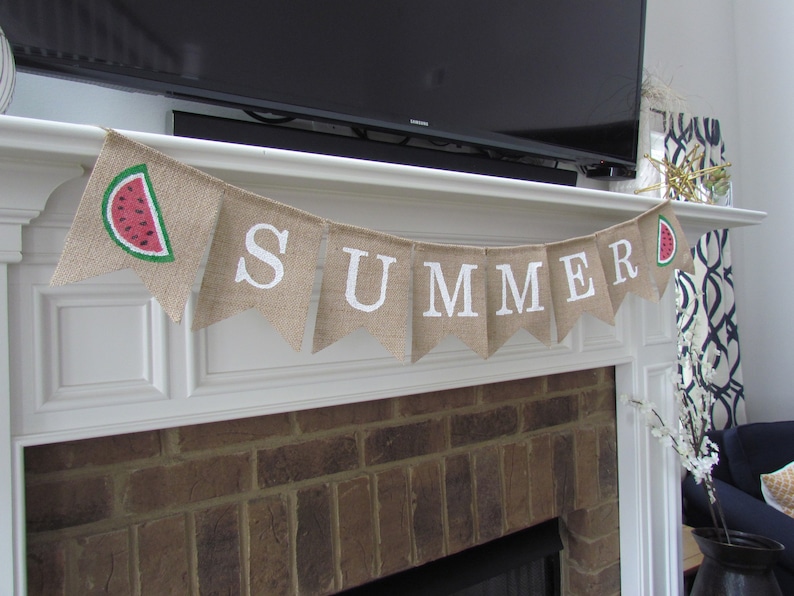 May include: A burlap banner with the word "SUMMER" in white letters and a watermelon slice graphic. The banner is hanging above a brick fireplace.