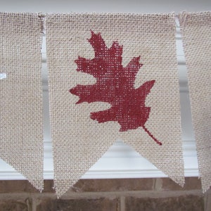 May include: A burlap banner with the word "Happy" and a red leaf design. The banner is strung together with white twine.
