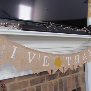 May include: A burlap banner with the words "Give Thanks" in white lettering. The banner is decorated with a yellow leaf and is hanging above a brick fireplace.
