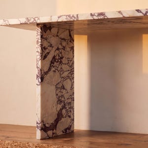 May include: A console table constructed from white marble with prominent, irregular deep purple veining. The piece features a thick, flat rectangular top supported by a single vertical slab leg, showcasing a continuous stone pattern throughout.