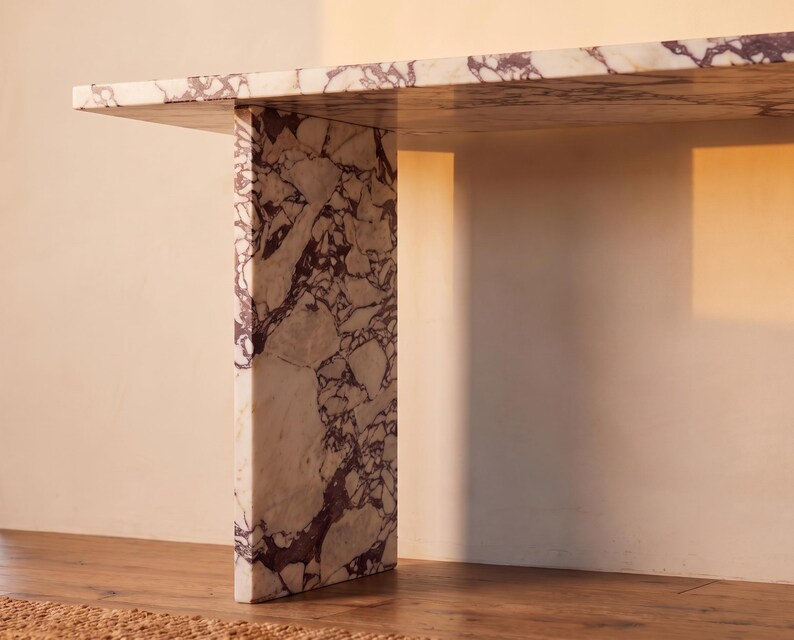 May include: A console table constructed from white marble with prominent, irregular deep purple veining. The piece features a thick, flat rectangular top supported by a single vertical slab leg, showcasing a continuous stone pattern throughout.