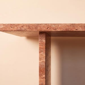 May include: A table constructed from reddish-brown travertine stone featuring a flat rectangular top surface supported by a single vertical slab leg. The natural stone material displays a porous, textured surface with visible pits and variations.