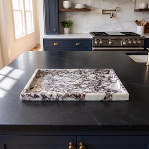 May include: A rectangular tray featuring a white and deep purple marble pattern with a polished finish. The tray has raised edges and a flat base, showcasing a distinct veined stone texture throughout the surface of the piece.