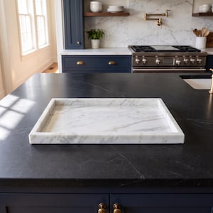 May include: A rectangular white marble tray featuring natural grey veining throughout the surface. The tray has a smooth, polished finish with raised edges on all four sides, providing a flat base for display or serving purposes.