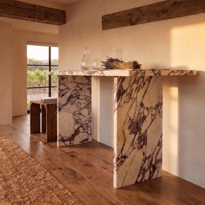 May include: A rectangular console table crafted from white marble with prominent deep purple veining. The table features a flat top supported by two vertical slab legs, showcasing a continuous stone pattern throughout the entire structure.