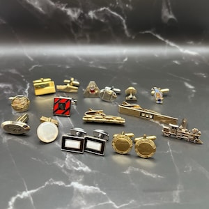 May include: A collection of assorted metal cufflinks and tie bars in various shapes and finishes, including gold-tone, silver-tone, and enamel designs. The set features geometric, circular, and novelty shapes, including a train-shaped tie bar.