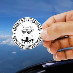 May include: A circular white sticker featuring a black line drawing of a dog wearing sunglasses and a spiked collar. The text reads FREIGHT DOGS ANONYMOUS and ORDER OF THE SLEEPLESS KNIGHTS with the acronym OOTSK centered at the bottom.