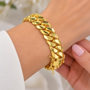 Op de afbeelding: Een gepolijste goudkleurige cuban schakelarmband met dikke, in elkaar grijpende ovale schakels met een hoogglanzend reflecterend oppervlak. De armband wordt vastgezet met een rechthoekig bakslot met een extra veiligheidssluiting aan de zijkant.