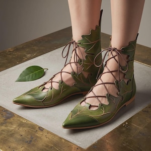 May include: A pair of olive green ankle boots featuring a pointed toe and a cutout design shaped like leaves. The boots are secured with thin brown laces that crisscross up the front and sides, creating a structured look with visible vein details.
