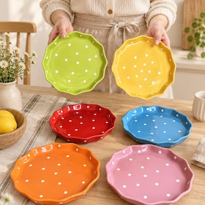 May include: A set of six ceramic plates with scalloped edges and a white polka dot pattern. The plates are available in lime green, yellow, red, blue, orange, and pink, each featuring a glossy finish and a circular shape with a raised rim.