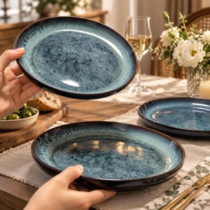 May include: A round ceramic dinner plate featuring a reactive glaze with a deep blue and teal center that transitions to a dark brown rim. The surface has a speckled, textured appearance with a glossy finish, showcasing a distinct color gradient.