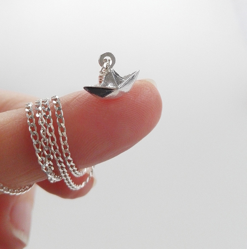 May include: A silver chain necklace with a small silver origami paper boat pendant.