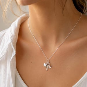 May include: A silver necklace with three charms: an anchor, a heart, and a small sailboat. The necklace is worn on a person wearing a white shirt.