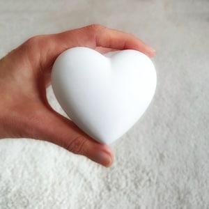 Könnte beinhalten: Ein weißes herzförmiges Objekt, das in einer Hand gehalten wird. Das Herz ist glatt und scheint aus Keramik zu sein.