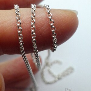 May include: Close-up of a delicate silver Rolo chain, held between fingers. The chain is composed of small, interconnected circular links. The text "Rolo Gliederkette 925 Sterling Silber" is visible at the bottom.